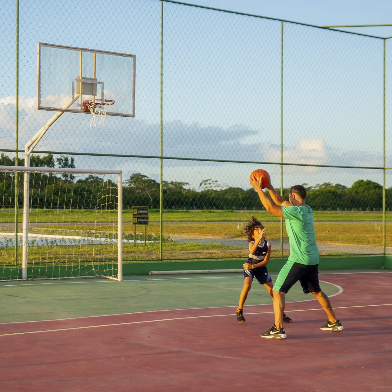 Adulto e criança jogando basquete na quadra poliesportiva